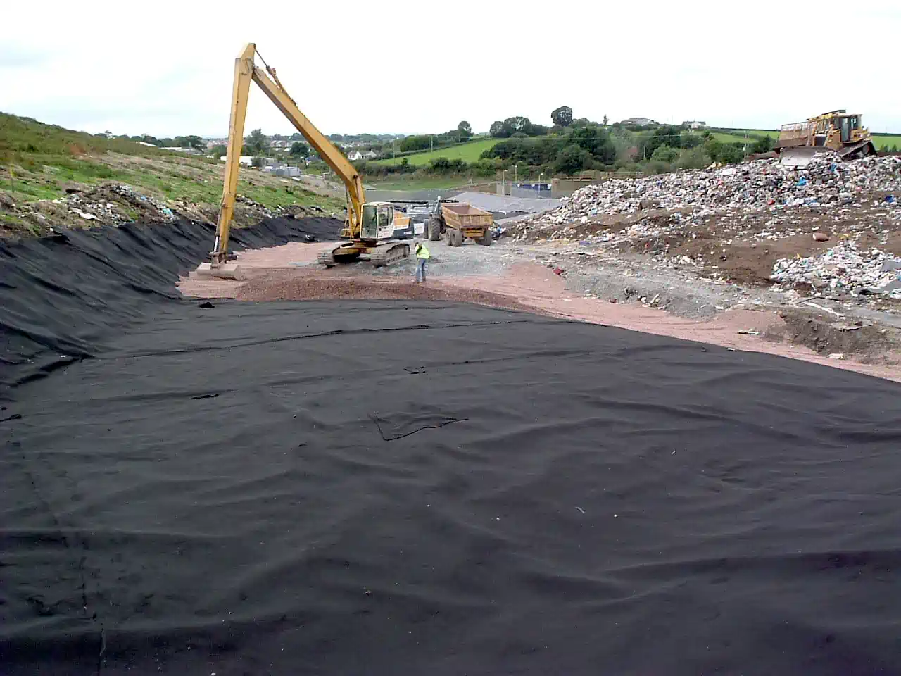 A welded HDPE Geomembrane Landfill lining during installation, showing the emplacement of a protective layer of stone, to act as a leachate drainage layer layer, prior to waste deposition filling.